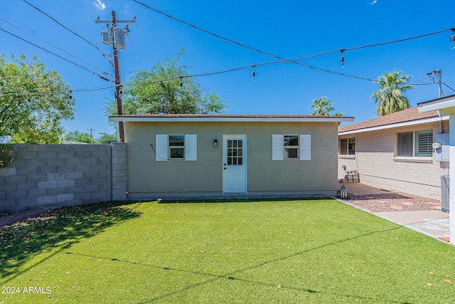 rear view of house featuring fence, an outdoor structure, a lawn, and stucco siding