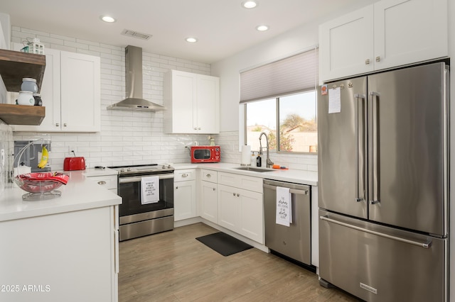 kitchen featuring visible vents, appliances with stainless steel finishes, white cabinets, a sink, and wall chimney range hood