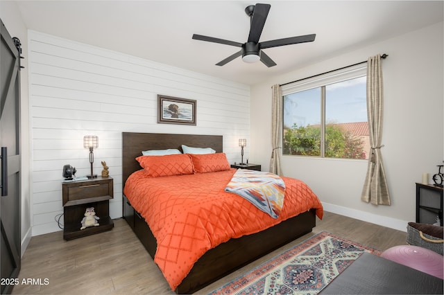 bedroom featuring ceiling fan, wooden walls, light wood-style flooring, and baseboards