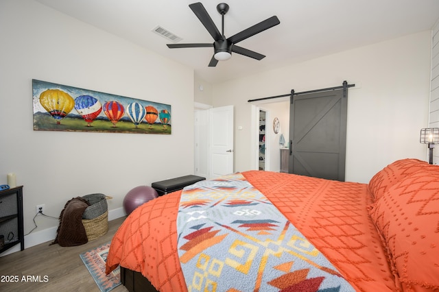 bedroom featuring a barn door, baseboards, visible vents, a ceiling fan, and wood finished floors