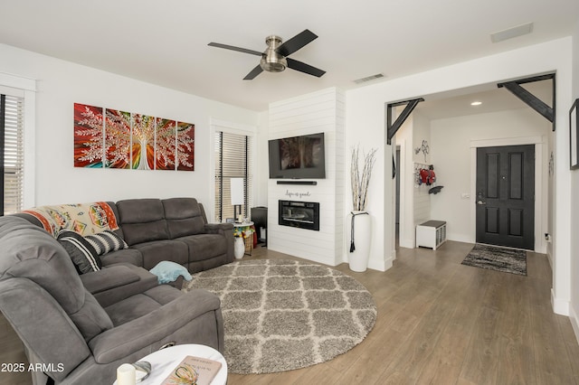 living area with a ceiling fan, a fireplace, visible vents, and wood finished floors