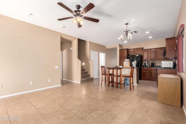 kitchen with hanging light fixtures, light tile patterned flooring, black refrigerator, ceiling fan with notable chandelier, and a center island