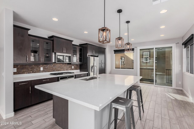 kitchen featuring sink, tasteful backsplash, an island with sink, pendant lighting, and appliances with stainless steel finishes