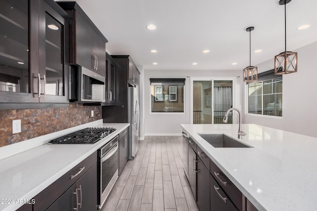 kitchen featuring sink, stainless steel appliances, light stone counters, backsplash, and decorative light fixtures