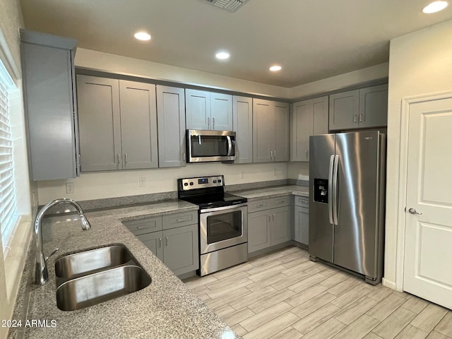 kitchen featuring stainless steel appliances, light wood-type flooring, gray cabinets, sink, and light stone counters