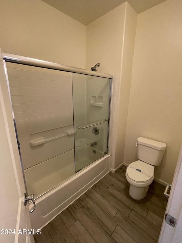 full bathroom with wood finish floors, baseboards, enclosed tub / shower combo, and toilet