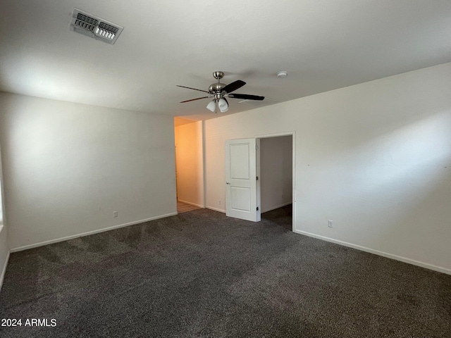 unfurnished room with a ceiling fan, visible vents, dark carpet, and baseboards