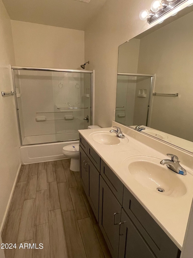 full bathroom with hardwood / wood-style floors, double vanity, combined bath / shower with glass door, and toilet