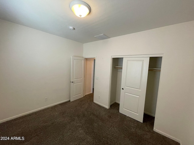 unfurnished bedroom with dark carpet and a closet