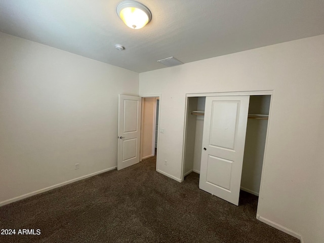 unfurnished bedroom with a closet, dark carpet, and baseboards