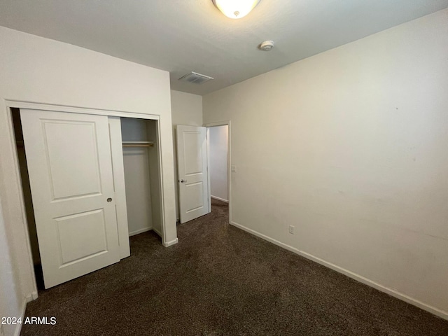 unfurnished bedroom with dark carpet and a closet