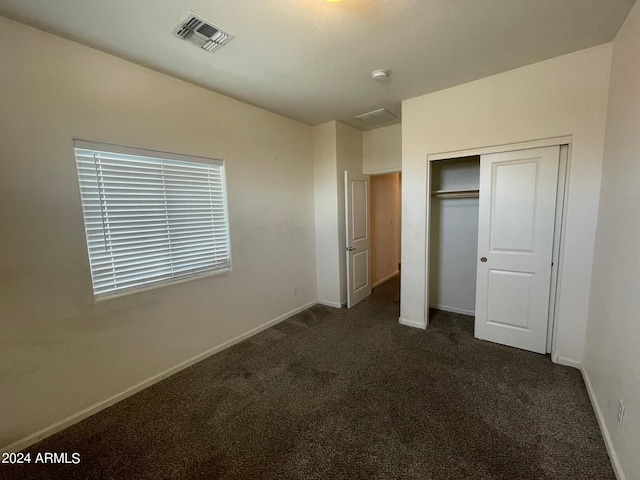 unfurnished bedroom with dark colored carpet and a closet