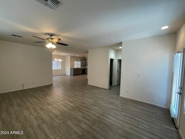 unfurnished living room with baseboards, visible vents, wood finished floors, and ceiling fan with notable chandelier