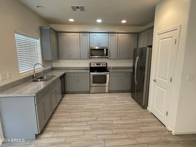 kitchen featuring gray cabinetry, appliances with stainless steel finishes, sink, and light stone countertops