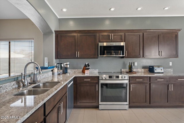 kitchen featuring dark brown cabinetry, light stone counters, stainless steel appliances, a sink, and recessed lighting