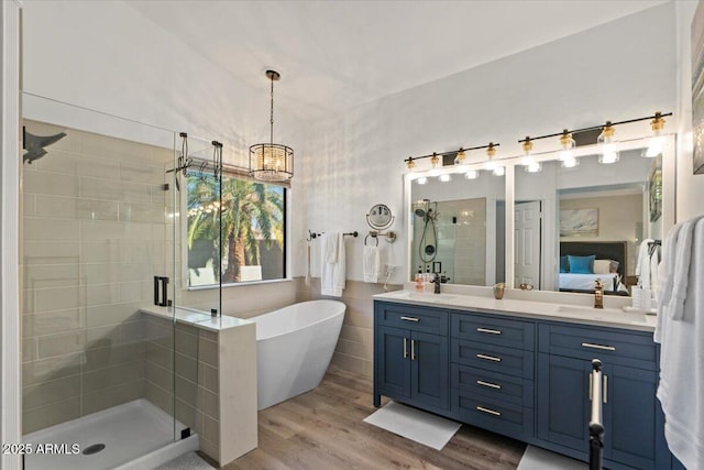 bathroom with connected bathroom, a sink, a shower stall, wood finished floors, and a freestanding tub