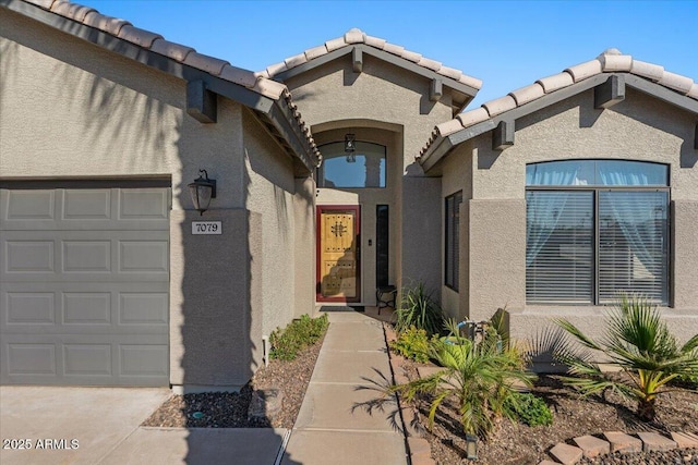 doorway to property with an attached garage, a tiled roof, and stucco siding