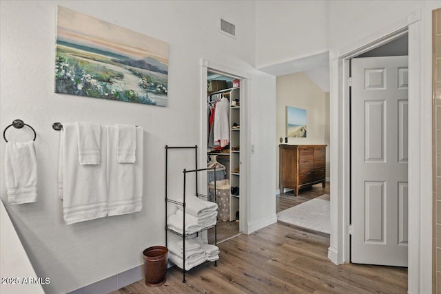 bathroom with a spacious closet, wood finished floors, visible vents, and baseboards