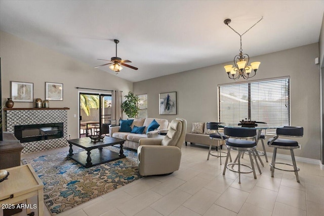 living area with baseboards, ceiling fan with notable chandelier, vaulted ceiling, and a tile fireplace