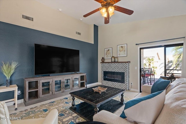 tiled living area with a fireplace, a ceiling fan, visible vents, vaulted ceiling, and baseboards