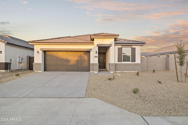 prairie-style home featuring a garage, driveway, a tiled roof, and stucco siding