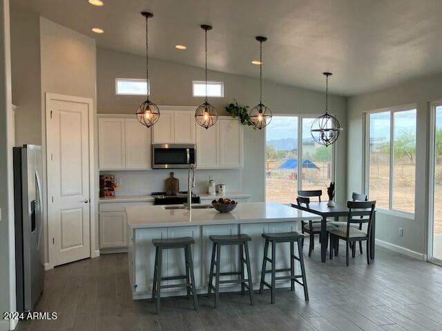 kitchen featuring appliances with stainless steel finishes, decorative light fixtures, lofted ceiling, and an island with sink