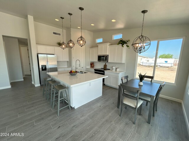 kitchen featuring a kitchen island with sink, white cabinetry, stainless steel appliances, and decorative light fixtures