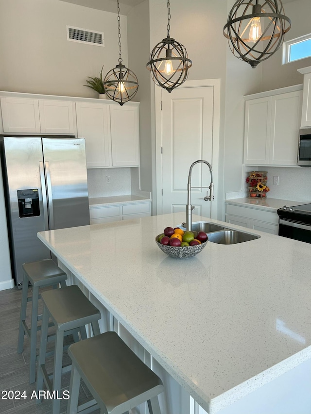 kitchen with white cabinetry, sink, stainless steel appliances, an island with sink, and pendant lighting