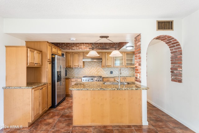 kitchen with stove, light stone counters, sink, stainless steel fridge with ice dispenser, and hanging light fixtures