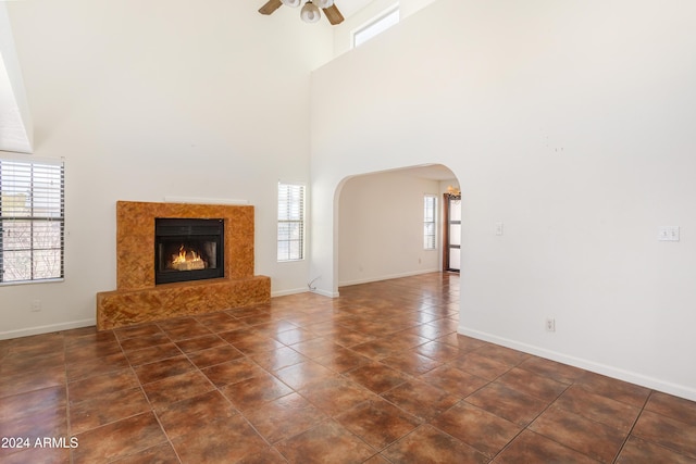 unfurnished living room featuring ceiling fan, a healthy amount of sunlight, a towering ceiling, and a premium fireplace