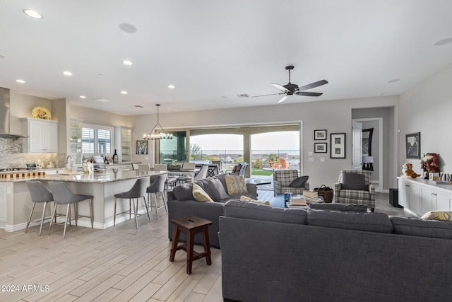 living area featuring light wood-style floors, recessed lighting, baseboards, and ceiling fan with notable chandelier