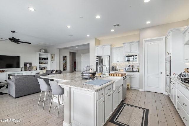 kitchen featuring a sink, visible vents, white cabinets, appliances with stainless steel finishes, and a center island with sink