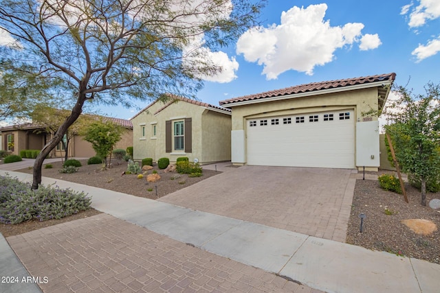 mediterranean / spanish house featuring decorative driveway, an attached garage, a tile roof, and stucco siding