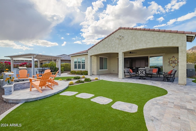 rear view of property featuring an outdoor living space with a fire pit, a patio, ceiling fan, a yard, and stucco siding