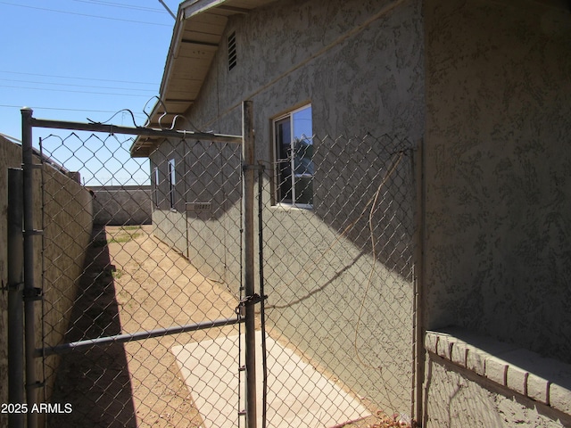 view of side of home featuring stucco siding, a gate, and fence