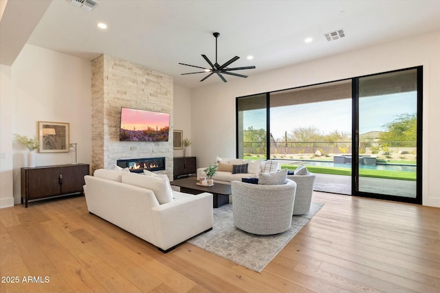 living room with ceiling fan, a stone fireplace, and light hardwood / wood-style floors