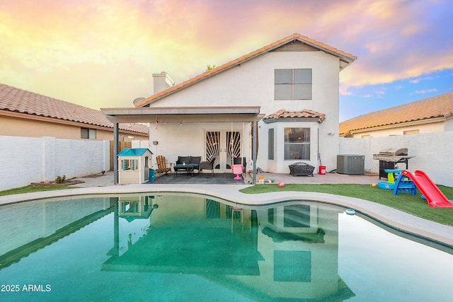 back house at dusk with a patio area, a fenced in pool, and central AC