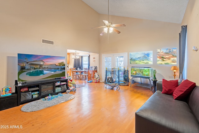 living room featuring ceiling fan with notable chandelier, a textured ceiling, hardwood / wood-style flooring, and high vaulted ceiling