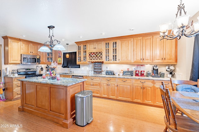 kitchen featuring appliances with stainless steel finishes, hanging light fixtures, a notable chandelier, light stone counters, and light hardwood / wood-style flooring