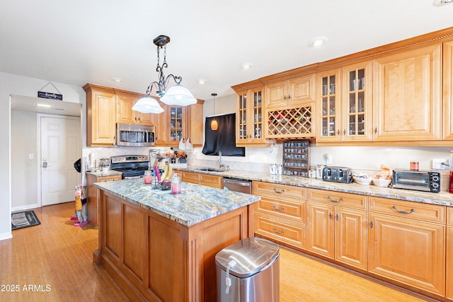 kitchen with light stone countertops, a kitchen island, stainless steel appliances, sink, and hanging light fixtures