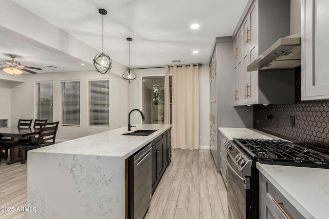 kitchen with tasteful backsplash, wall chimney range hood, light wood-style floors, stainless steel appliances, and a sink