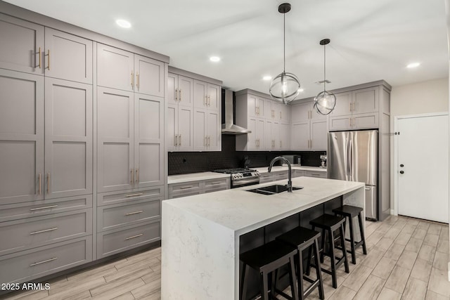 kitchen with a sink, gray cabinetry, appliances with stainless steel finishes, wall chimney exhaust hood, and tasteful backsplash