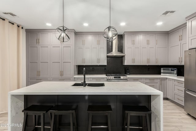 kitchen featuring visible vents, gray cabinets, a sink, appliances with stainless steel finishes, and wall chimney range hood