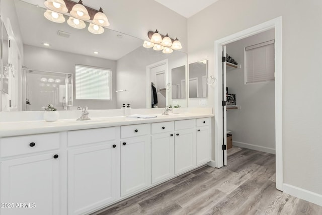 bathroom featuring a shower stall, wood finished floors, double vanity, and baseboards