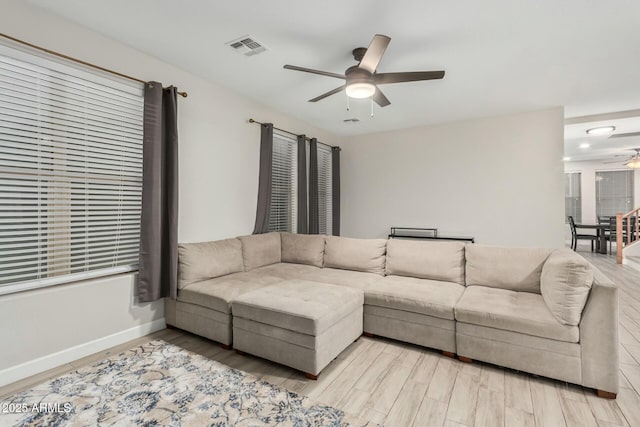 living room with light wood-style flooring, a ceiling fan, visible vents, and baseboards