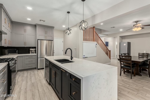 kitchen featuring visible vents, a center island with sink, gray cabinets, stainless steel appliances, and a sink