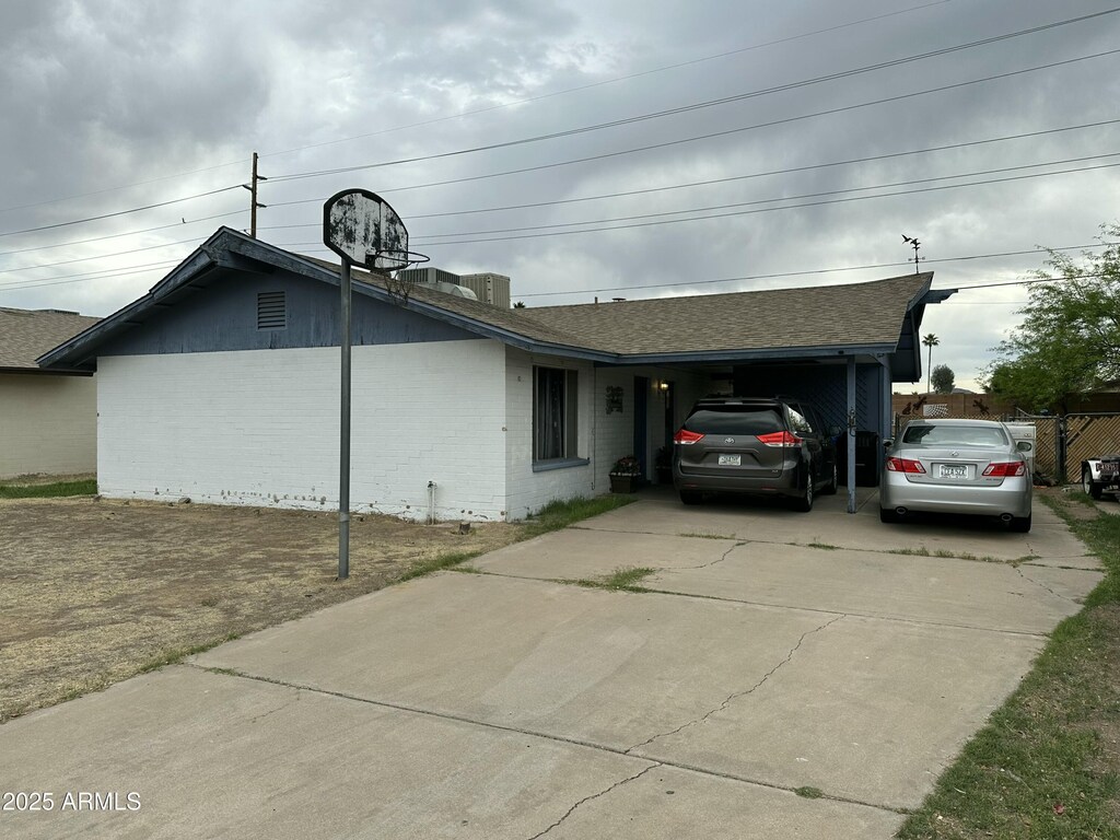 view of home's exterior featuring brick siding, an attached carport, roof with shingles, and concrete driveway