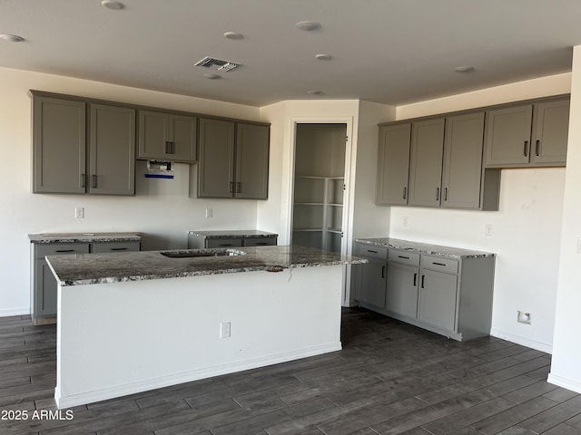 kitchen featuring a center island, dark wood-style flooring, visible vents, and dark stone countertops