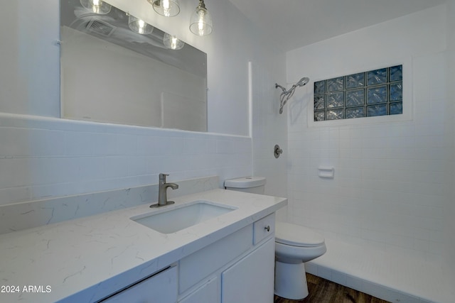 bathroom featuring backsplash, a tile shower, vanity, hardwood / wood-style floors, and toilet