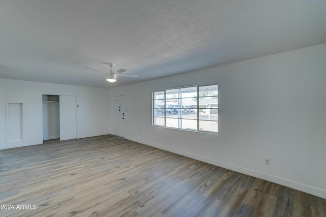 unfurnished room with a textured ceiling, light wood-type flooring, and ceiling fan